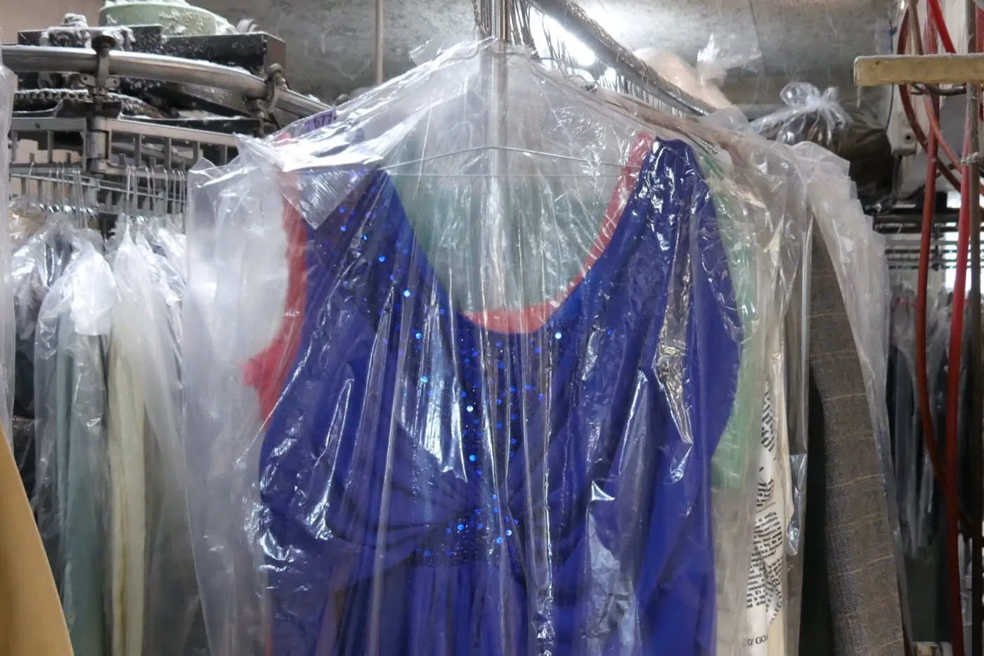 Vêtements protégés sous housse sur le convoyeur du Pressing Belle Allure